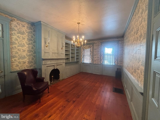 unfurnished dining area featuring a wainscoted wall, a notable chandelier, ornamental molding, dark wood finished floors, and wallpapered walls