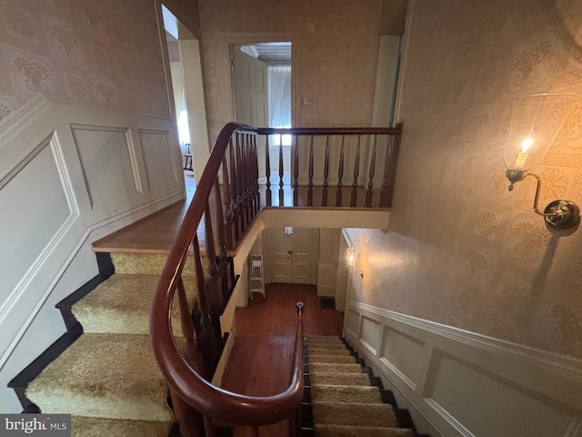 stairway with a decorative wall, wallpapered walls, and a wainscoted wall