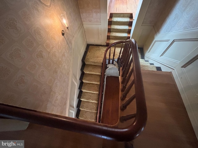 staircase featuring a decorative wall, wainscoting, and wallpapered walls