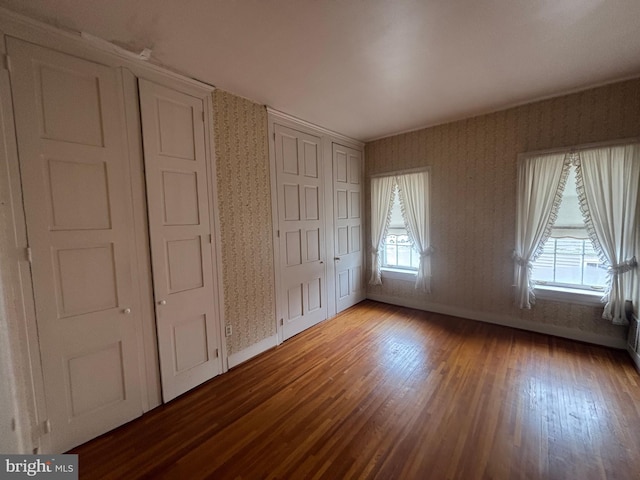 unfurnished bedroom featuring multiple windows, wood finished floors, and wallpapered walls