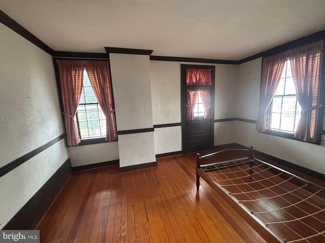 empty room featuring crown molding, plenty of natural light, baseboards, and wood-type flooring