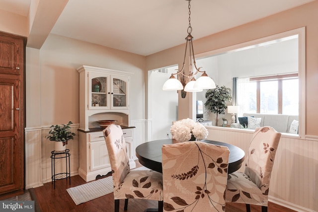 dining room featuring dark wood finished floors, a wainscoted wall, a decorative wall, and an inviting chandelier