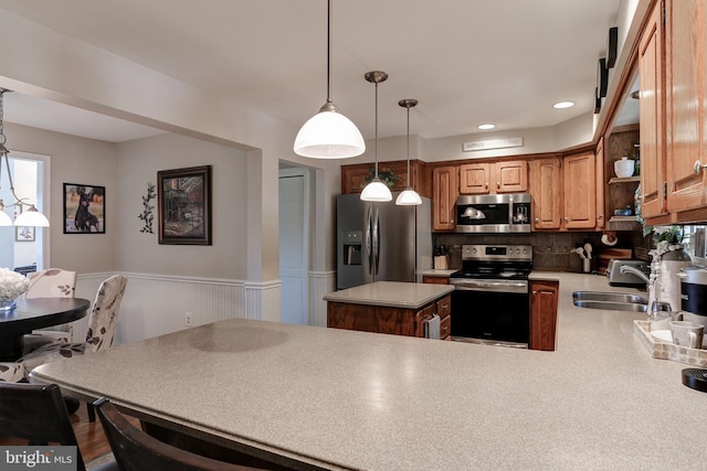 kitchen with a wainscoted wall, a sink, decorative light fixtures, appliances with stainless steel finishes, and light countertops