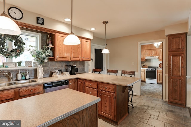 kitchen with stone finish floor, under cabinet range hood, a sink, gas range oven, and a peninsula