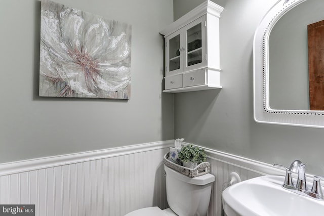 half bath with a wainscoted wall, toilet, and a sink