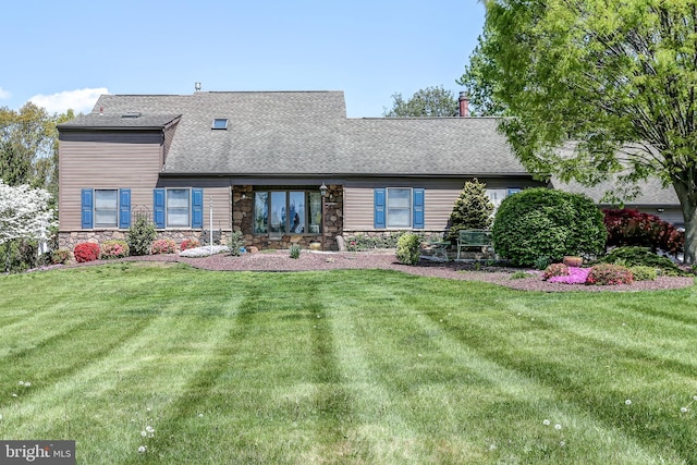 rear view of property with stone siding, a yard, and roof with shingles