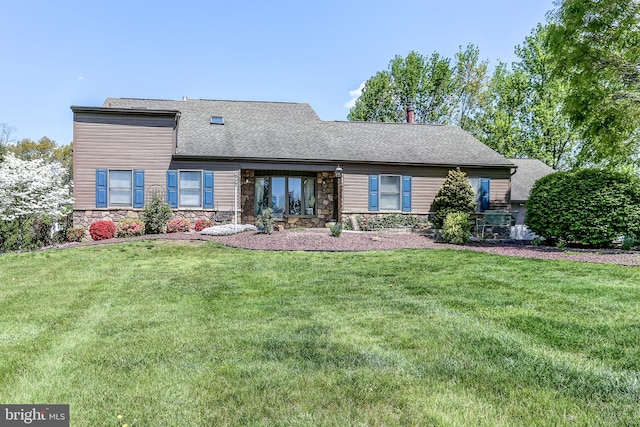 rear view of property featuring a yard, stone siding, and roof with shingles