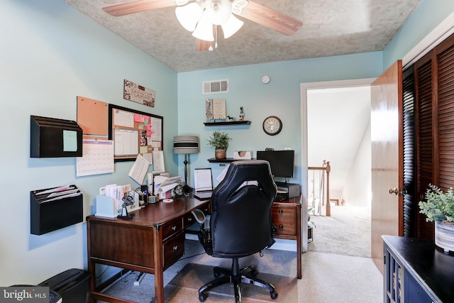 carpeted office space featuring visible vents, a textured ceiling, and a ceiling fan