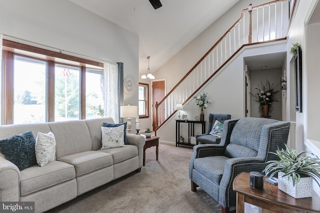 living area featuring light carpet, stairway, ceiling fan with notable chandelier, and a high ceiling