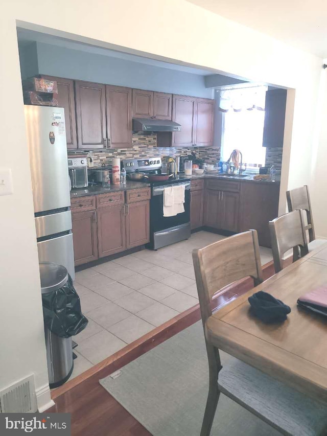 kitchen featuring visible vents, under cabinet range hood, dark countertops, appliances with stainless steel finishes, and decorative backsplash