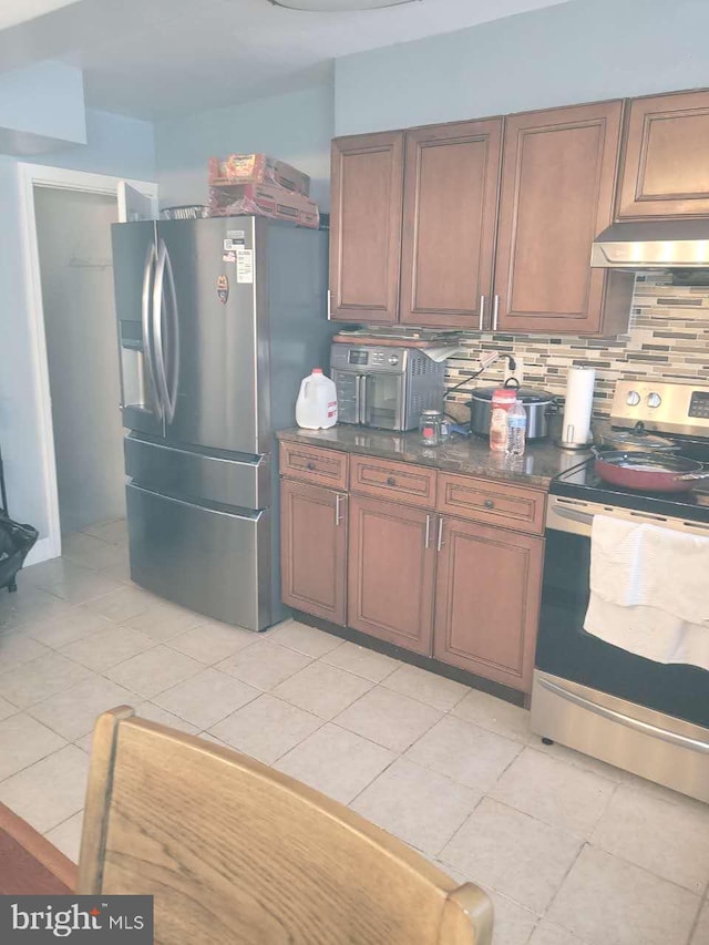 kitchen featuring decorative backsplash, under cabinet range hood, light tile patterned floors, and appliances with stainless steel finishes