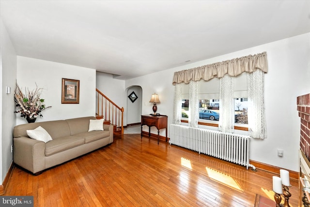 living room with stairway, wood-type flooring, baseboards, and radiator heating unit