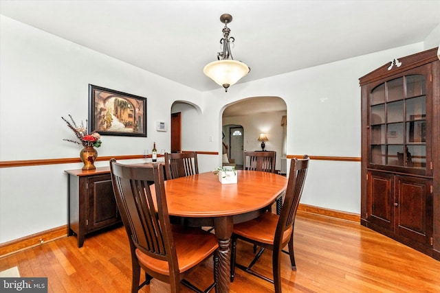 dining area featuring arched walkways, light wood-style flooring, and baseboards