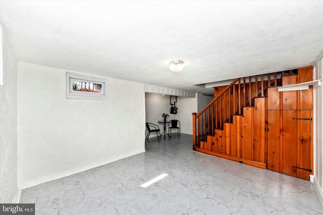 basement featuring a textured ceiling, stairs, and a textured wall