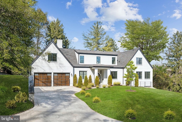 modern farmhouse featuring a front lawn, concrete driveway, stucco siding, a chimney, and a garage