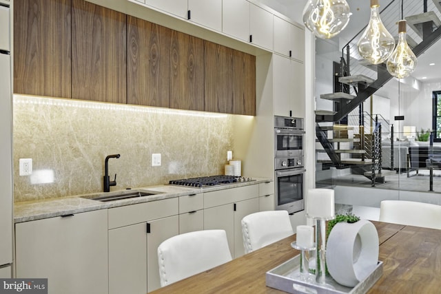 kitchen with stainless steel appliances, decorative backsplash, hanging light fixtures, a sink, and white cabinetry