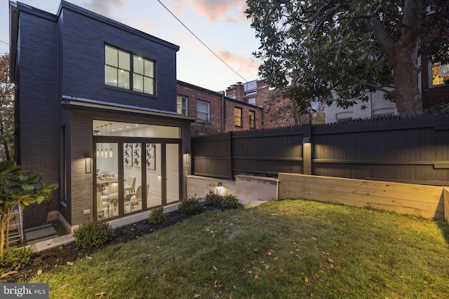 back of house at dusk featuring a yard, fence, and brick siding