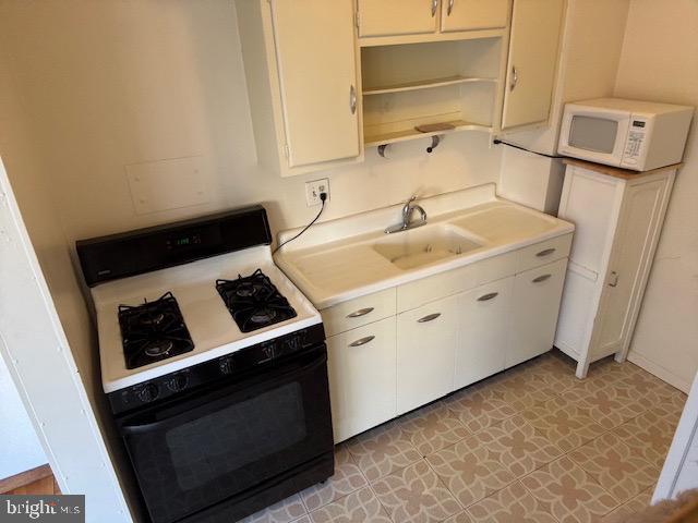 kitchen featuring white microwave, open shelves, a sink, light countertops, and gas range