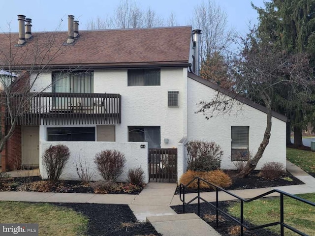 view of front of home featuring a fenced front yard, roof with shingles, stucco siding, a balcony, and a gate