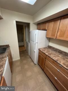 kitchen featuring stone counters, brown cabinets, and freestanding refrigerator