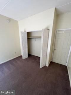 unfurnished bedroom with dark colored carpet and a closet