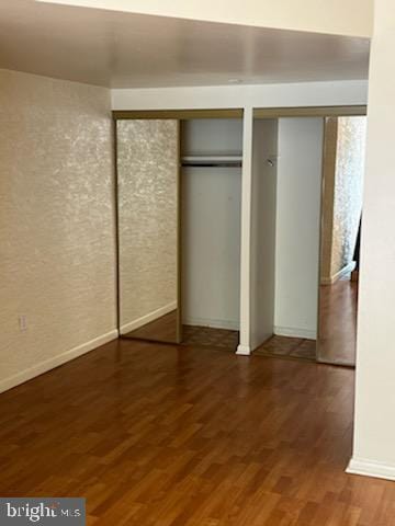 unfurnished bedroom featuring wood finished floors, baseboards, and two closets