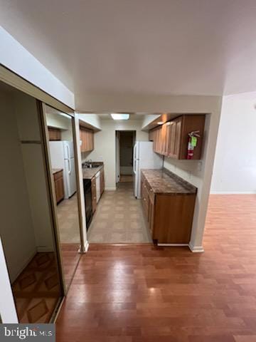 kitchen featuring light wood finished floors, brown cabinetry, and freestanding refrigerator