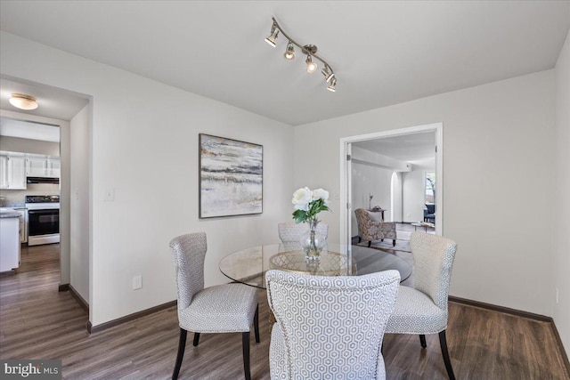 dining room featuring track lighting, baseboards, and dark wood-type flooring