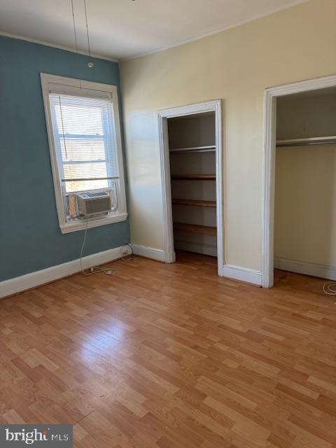 unfurnished bedroom with multiple closets, ornamental molding, cooling unit, light wood finished floors, and baseboards