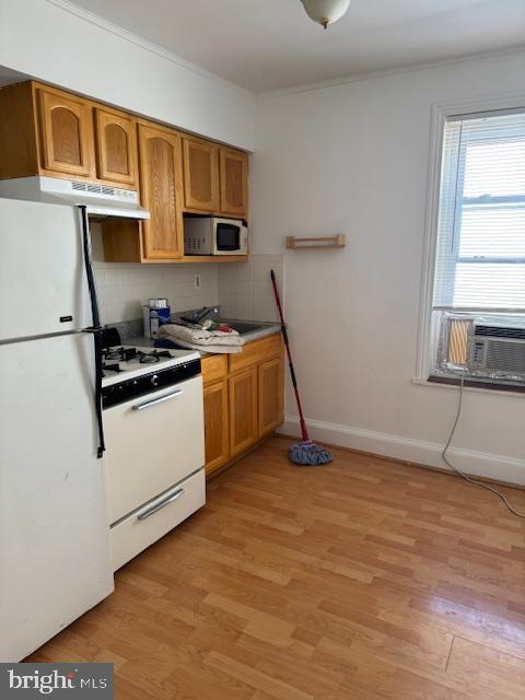 kitchen featuring light wood-style flooring, ornamental molding, under cabinet range hood, backsplash, and white appliances