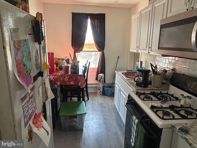 kitchen featuring stainless steel microwave, backsplash, freestanding refrigerator, wood finished floors, and gas stove