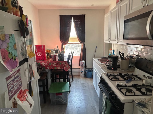 kitchen featuring light wood-type flooring, stainless steel microwave, range with gas stovetop, tasteful backsplash, and white cabinetry