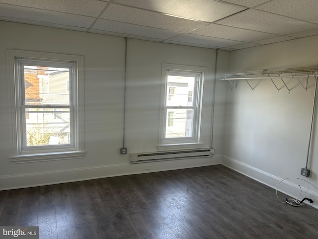 interior space with a baseboard heating unit, multiple windows, a paneled ceiling, and dark wood-style flooring