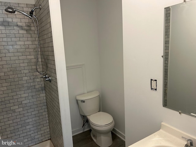 full bath featuring vanity, wood finished floors, baseboards, tiled shower, and toilet