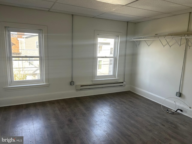 interior space with a wealth of natural light, a drop ceiling, a baseboard heating unit, and dark wood-style flooring