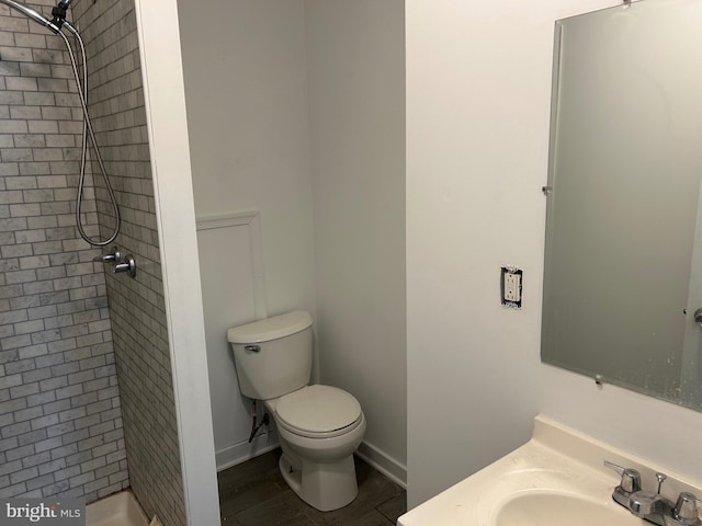 bathroom with toilet, tiled shower, vanity, and baseboards