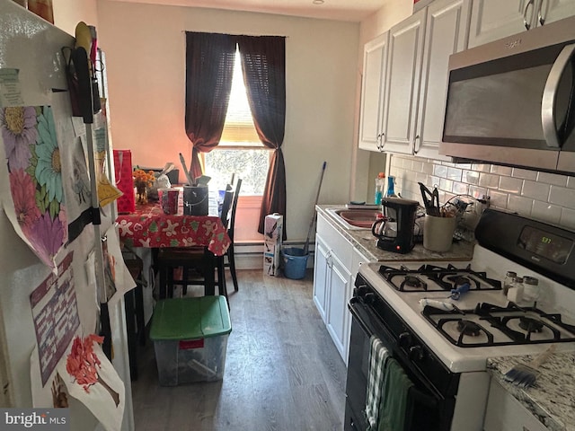 kitchen with wood finished floors, decorative backsplash, gas range oven, white cabinetry, and stainless steel microwave