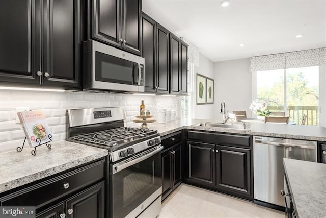 kitchen featuring backsplash, dark cabinets, light countertops, appliances with stainless steel finishes, and a sink