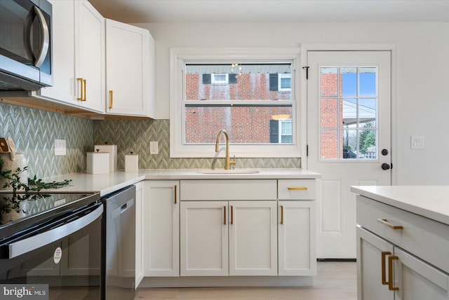 kitchen with a sink, backsplash, appliances with stainless steel finishes, white cabinets, and light countertops