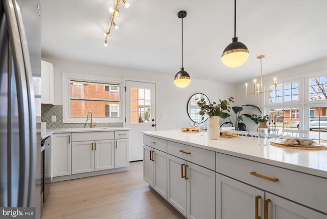 kitchen featuring light wood-type flooring, a sink, tasteful backsplash, stainless steel appliances, and light countertops