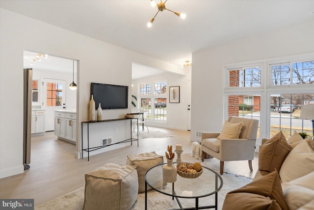 living room featuring visible vents, baseboards, light wood-style floors, and an inviting chandelier