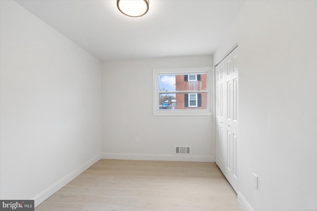 empty room featuring visible vents, light wood-type flooring, and baseboards