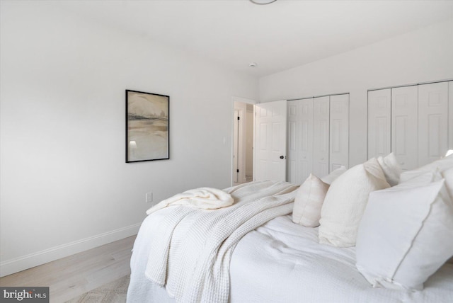 bedroom featuring light wood finished floors, two closets, and baseboards