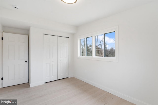 unfurnished bedroom with light wood-type flooring, baseboards, and a closet