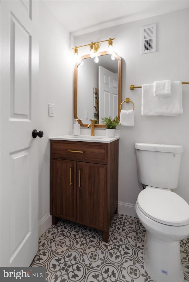 half bathroom featuring vanity, baseboards, visible vents, tile patterned floors, and toilet