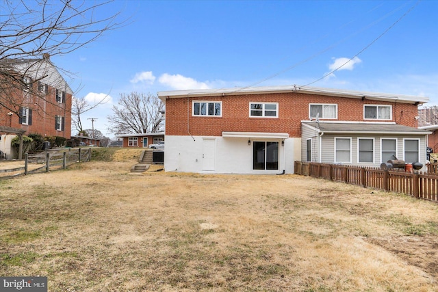 rear view of house featuring stucco siding, fence, brick siding, and a lawn