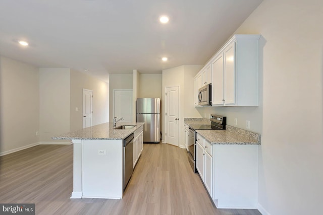 kitchen with an island with sink, a sink, appliances with stainless steel finishes, white cabinetry, and light wood-type flooring