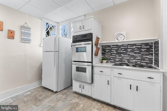 kitchen with baseboards, light countertops, a paneled ceiling, appliances with stainless steel finishes, and white cabinetry