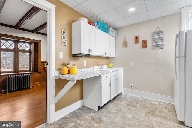 kitchen with radiator, white cabinetry, freestanding refrigerator, and a sink