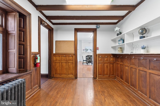 kitchen featuring beamed ceiling, a wainscoted wall, light wood-type flooring, radiator heating unit, and open shelves